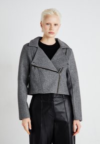 Gray cropped jacket made of textured fabric, featuring a double-breasted design, lapel collar, and front zipper. Styled with black trousers.