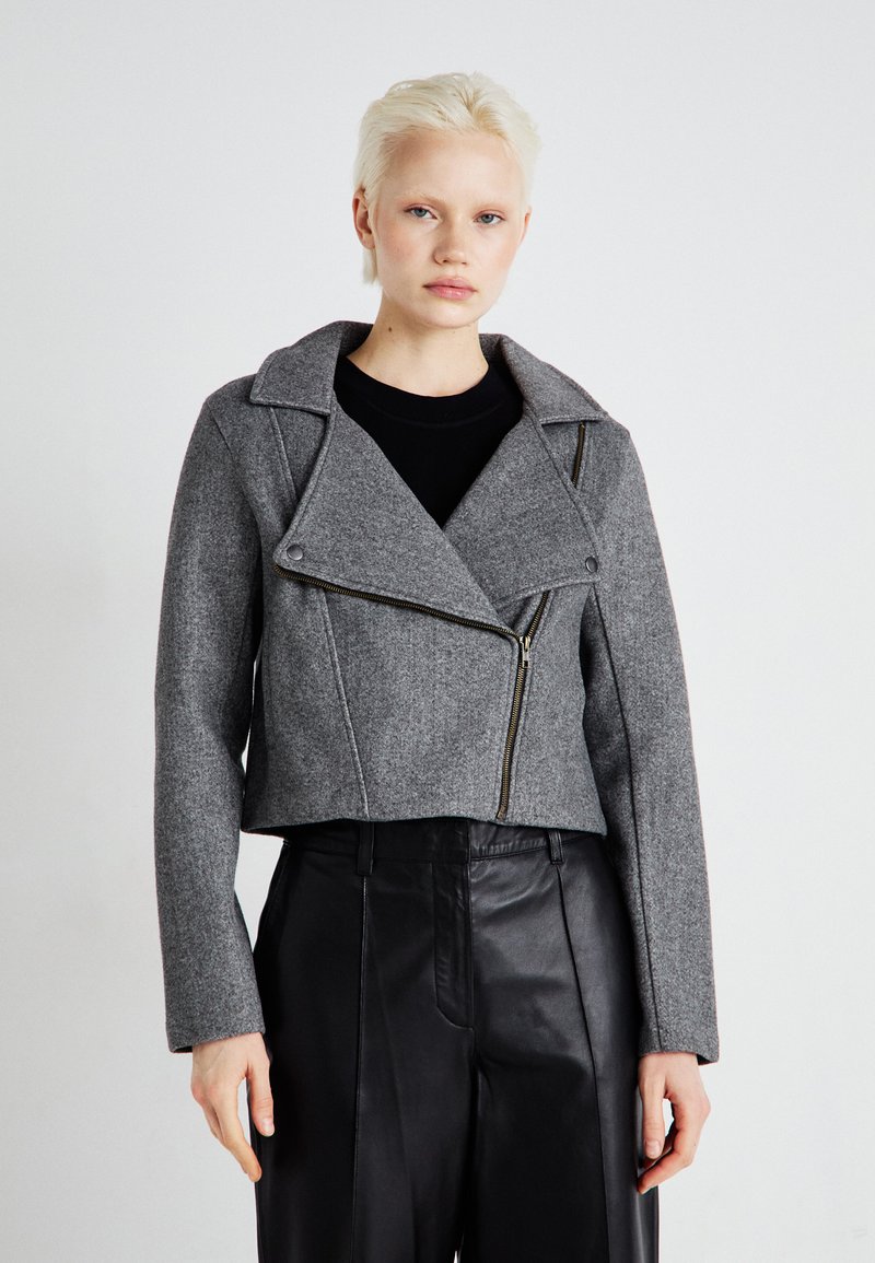 Gray cropped jacket made of textured fabric, featuring a double-breasted design, lapel collar, and front zipper. Styled with black trousers.