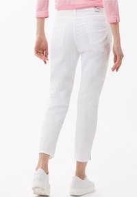 Bílé džíny se slim fit, s zadními kapsami, rozstřiženým lemem a značkovým štítkem. Spárovány s bílými teniskami.