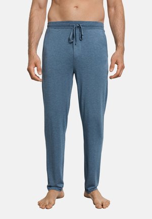 Man draagt blauwe loungebroek met trekkoord, staat blootsvoets tegen een effen witte achtergrond.