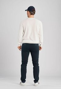 Bílý svetr, tmavě modré kalhoty a námořnická čepice. Svetr má jednoduchý design, zatímco kalhoty mají kapsy. Boty jsou bílé s námořnickými akcenty.