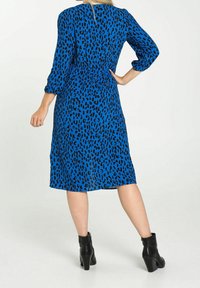 Vestido azul con un estampado de leopardo negro, mangas tres cuartos y un corte a media longitud, combinado con botas negras hasta el tobillo.