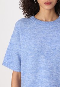 Suéter azul claro de mangas curtas feito de tecido macio, com decote redondo e textura subtil. Sem padrões ou peças de metal visíveis.