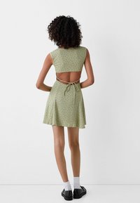 Crop top verde con motivo, dotato di aperture sul retro e dettaglio a fiocco, abbinato a una mini gonna svasata, progettato per una silhouette aderente.