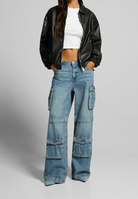 Svart faux läder bomberjacka med ribbad mudd, tillsammans med ljusblå vida cargoj jeans med stora framfickor och sömmar.