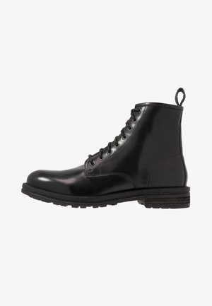 Bottine en cuir noir avec bout arrondi, laçage latéral, six œillets et semelle en caoutchouc texturée. Dotée d'une bande de tirage au talon.