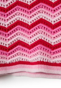 Copricostume all'uncinetto con motivi a zigzag in tonalità di rosso, rosa e bianco. Orlo a costine e trama a giorno.