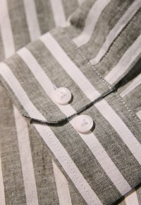 Gestreifte Hemd mit abwechselnd grünen und weißen Streifen, mit Kragen und zwei weißen Knöpfen an den Manschetten, die mit feinen Nähten gearbeitet sind.