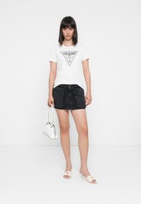 White cotton t-shirt with a triangular graphic, paired with a black denim skirt featuring patch pockets, and white heeled mules with gold accents.