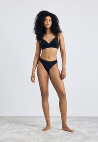 Zwarte bikini set met een V-hals bralette en bijpassende textuurstring. Glad stof met een minimalistisch ontwerp, zonder zichtbare hardware.