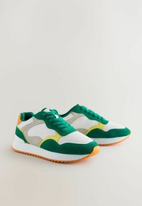 Adidași verzi și albi, confecționați din materiale din suede și plasă, cu o talpă căptușită, călcâie și talpă exterioară în contrast de portocaliu și accente galbene.