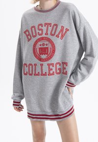 Šedá mikina s nápisem "BOSTON COLLEGE" v červeném písmu, kruhovým emblémem a červenými proužkovými akcenty na manžetách a spodu.