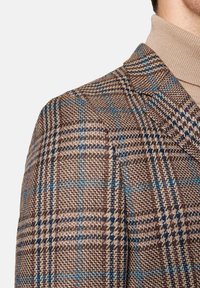 Brązowa i niebieska marynarka w kratę, z fakturowanym splotem, ostrymi klapami i subtelnymi detalami w wzorze. Tkanina prezentuje ciepłe odcienie.