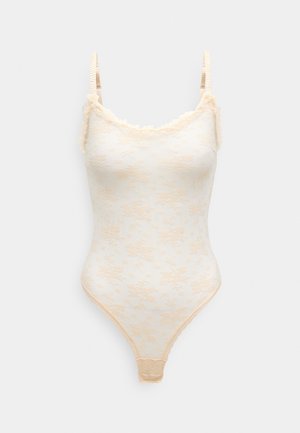 Body z koronką w delikatnym kremowym kolorze z kwiatowym wzorem, falbaniaste dekolt, cienkie regulowane ramiączka; dopasowany krój z wycięciem typu thong.
