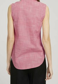 Ärmellose rosa Bluse mit gewebtem Strukturmuster, abgerundetem Saum und dezentem Kragen. Hergestellt aus leichtem Stoff.