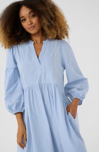 Light blue cotton dress with a V-neck, puffed sleeves, scalloped trim, and gathered waist. Includes hidden pockets for functionality.