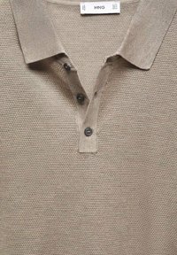 Polo en tricot beige texturé avec trois boutons sombres et un col plié, taille moyenne étiquetée par la marque MNG.