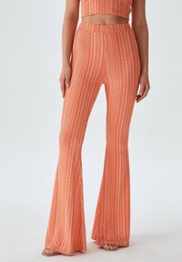 Uitlopende, hooggewaisted broeken in levendig oranje met verticale witte strepen en een textuurpatroon. Materiaal is zacht, lichtgewicht en rekbaar.