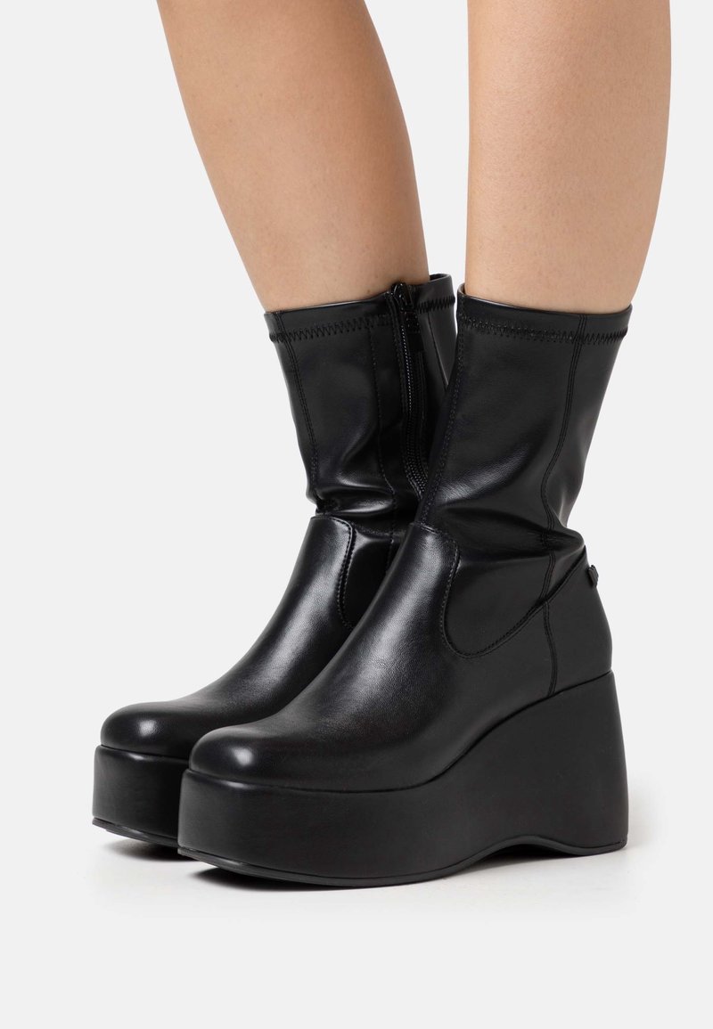 Bottes compensées noires montant jusqu'aux chevilles, en cuir lisse. Dotées d'une fermeture éclair latérale et d'un bout rond, avec une semelle épaisse à plateforme.