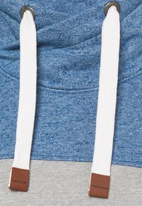 Blauer und grauer Hoodie mit strukturiertem Strickmuster, weißen Kordeln und braunen Lederlogo-Akzenten an den Enden.