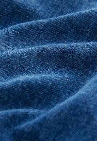 Tumedat sinine denimkangas, millel on tekstuuriga pind, kerge sära ja nähtava kudumisega, luues pehme, lainelise välimuse.
