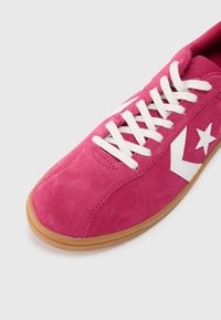 Sneaker in suede rosa con lacci bianchi e logo a stella. Presenta una suola in gomma e una punta rotonda, con dettagli di cucitura lungo la parte superiore.