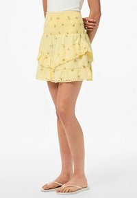 Falda amarilla de volantes con patrones florales, cintura fruncida y dobladillo con forma de ola. Fabricada con tejido ligero.