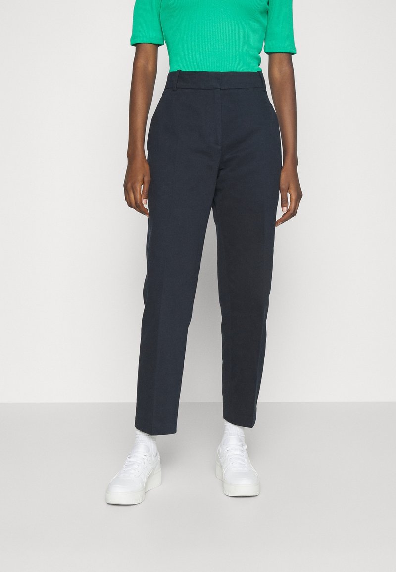 Marineblauwe high-waisted broeken van katoen, met een recht been ontwerp, zijzakken en een gladde textuur. Gecombineerd met witte sneakers.