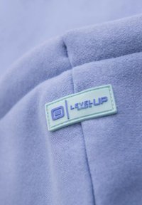 Tissu bleu clair avec une finition texturée, arborant un patch rectangulaire vert menthe portant l'inscription "LEVEL UP" en texte violet.