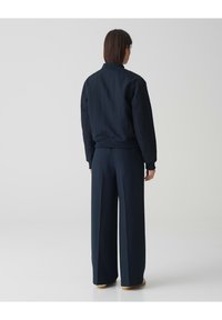 Dunkelblaues Bomberjackett mit gerippten Bündchen und Saum, kombiniert mit hoch taillierten weiten Hosen. Glatte Textur, minimalistisches Design.