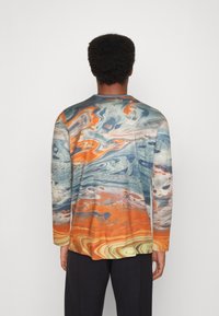 Pitkähihainen paita, jossa on pyörivä kuviokuva sinisen, oranssin ja beigeen sävyissä, ribbaamalla varustettu kaulus ja hihat. Valmistettu pehmeästä, teksturoidusta kankaasta.