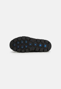 Semelle de chaussure noire présentant un motif d'accents circulaires avec des reflets bleus et des rainures texturées pour une meilleure traction. Matériau en caoutchouc durable.