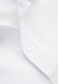 Close-up af hvid skjortekrave med synlig knap og tekstureret stofdetalje.