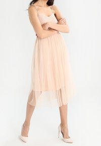 Světlé růžové šaty na tenkých ramínkách s přiléhavým korzetem a vrstvenou tylovou sukní. Sukně je poloprůhledná a sahá po polovinu lýtek.