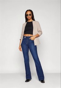 Blazer bege sobre um top crop preto, combinado com jeans flare azul escuro. O conjunto apresenta uma silhueta ajustada e um design minimalista.