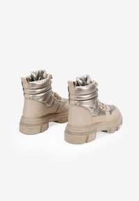 Botas de tobillo beige y plateadas metálicas con cuello acolchado, diseño con cordones, suela gruesa y suela de goma texturizada.