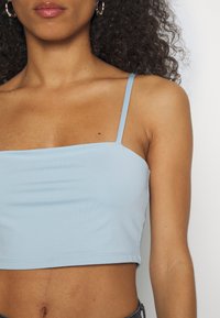 Top cropped azul claro com alças finas, feito de um tecido liso e elástico. Apresenta um decote quadrado e uma bainha que termina na cintura.