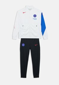 Le survêtement Nike se compose d'une veste blanche à fermeture éclair avec des accents rouges et bleus, et d'un pantalon noir avec un logo bleu et un swoosh rouge Nike. Tissu texturé.