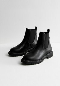 Czarne skórzane botki za kostkę z elastycznymi panelami, zaokrąglonymi noskami oraz teksturowaną gumową podeszwą. Białe przeszycia ozdabiają krawędzie butów.