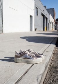 Ζευγάρι μεταλλικά sneakers με πλατφόρμα τοποθετημένα σε τσιμεντένιο πεζοδρόμιο δίπλα σε πεζοδρόμιο σε αστικό δρόμο.