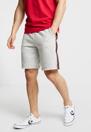Graue Sportshorts mit schwarzen und roten Seitenstreifen, aus weichem Baumwollmischgewebe, kombiniert mit weißen Sneakers und einem roten T-Shirt.