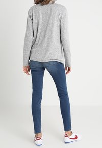 Maglietta grigia a maniche lunghe in maglia, jeans blu slim-fit e sneakers bianche con dettagli rossi. Tessuto minimal; vestibilità casual.
