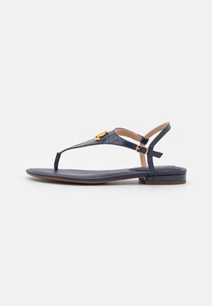 Marineblå flad sandal med tårem og guldfarvet spænde samt justerbar ankelrem på hvid baggrund.
