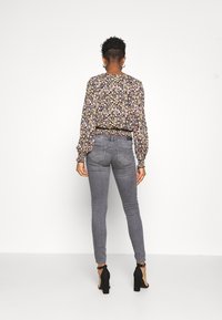 Blusa floral de manga longa em preto, com cintura franzida e punhos elásticos, combinada com jeans skinny cinza e tacões pretos.