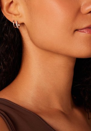 Zilveren hoepelogen met een gebogen ontwerp, voorzien van een rij heldere rhinestones voor extra detail, gedragen in een oor.