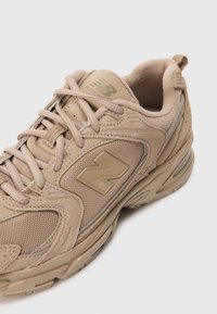 Beige Sportschuh aus Netz- und Wildledermaterial, mit abgerundeter Zehenpartie, dicken Sohlen und Logo an der Seite. Schnürsenkel und gepolsterter Kragen sind enthalten.
