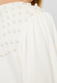Maglione bianco lavorato a maglia con tessuto testurizzato e righe di perle finte sulle spalle e maniche a palloncino per maggiore volume.