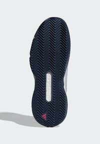 Sula på marinblå sportskor med fiskbensmönster, vit mellansula synlig genom urtag, och liten rosa triangel-logotyp nära hälen.