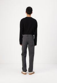 Grå denimbukser med rett snitt, kombinert med en svart langermet skjorte, sett fra baksiden, med standard lommer og minimal detaljering.