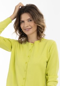 Cardigan giallo brillante con scollatura arrotondata, chiusura a bottoni e polsini a costine. Il tessuto appare morbido con una superficie liscia.